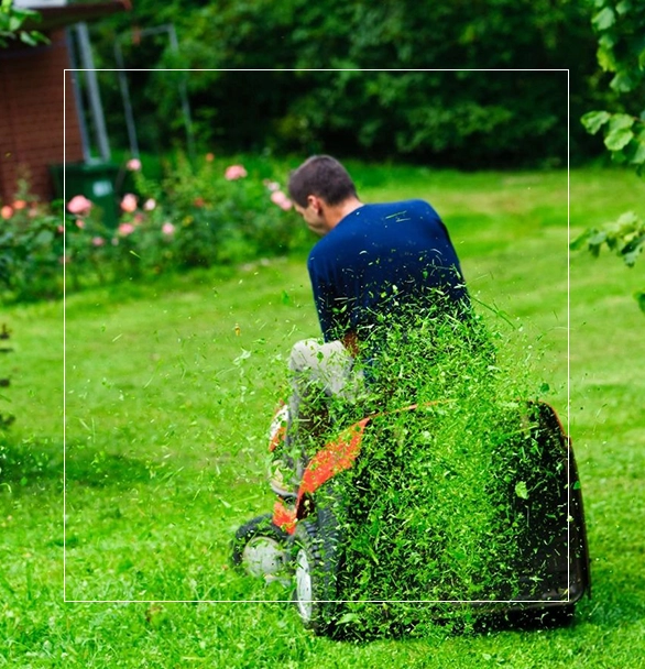 A man sitting on the grass with a lawn mower.